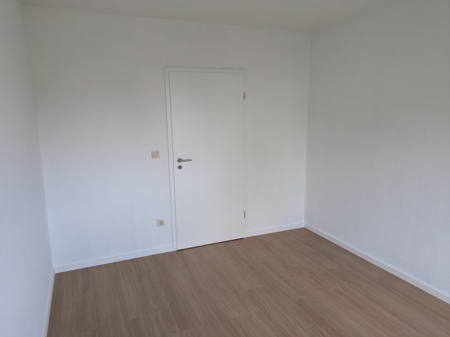 Leere, helle Raum mit Holzfußboden und geschlossener Tür.
