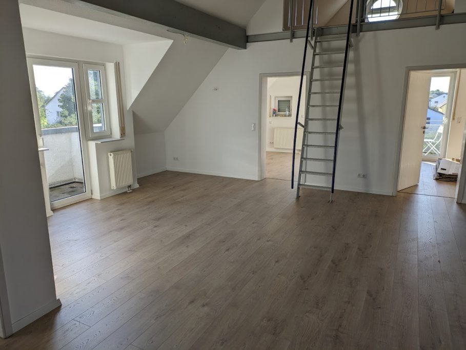 Geräumiger, lichtdurchfluteter Raum mit Holzfußboden und Zugang zu Balkontüren.