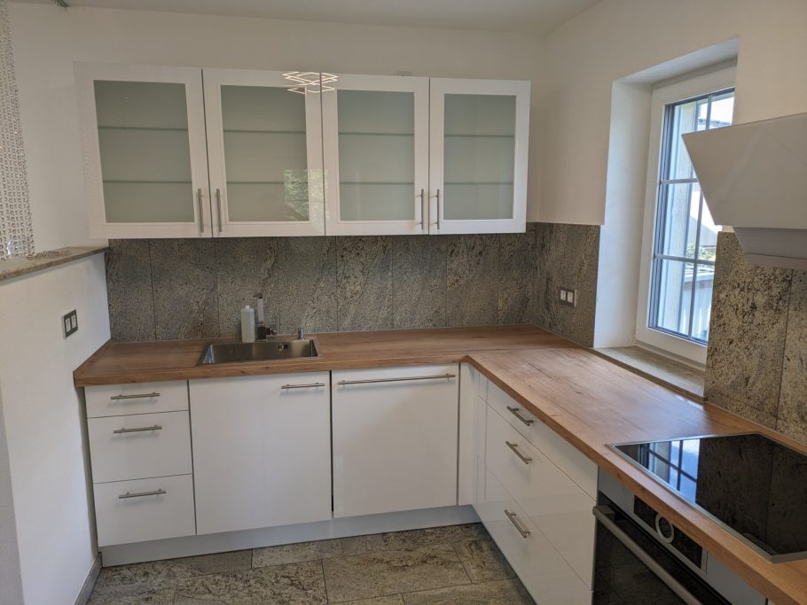 Moderne Küche mit weißen Schränken, Holzarbeitsplatte und neuem Fenster.